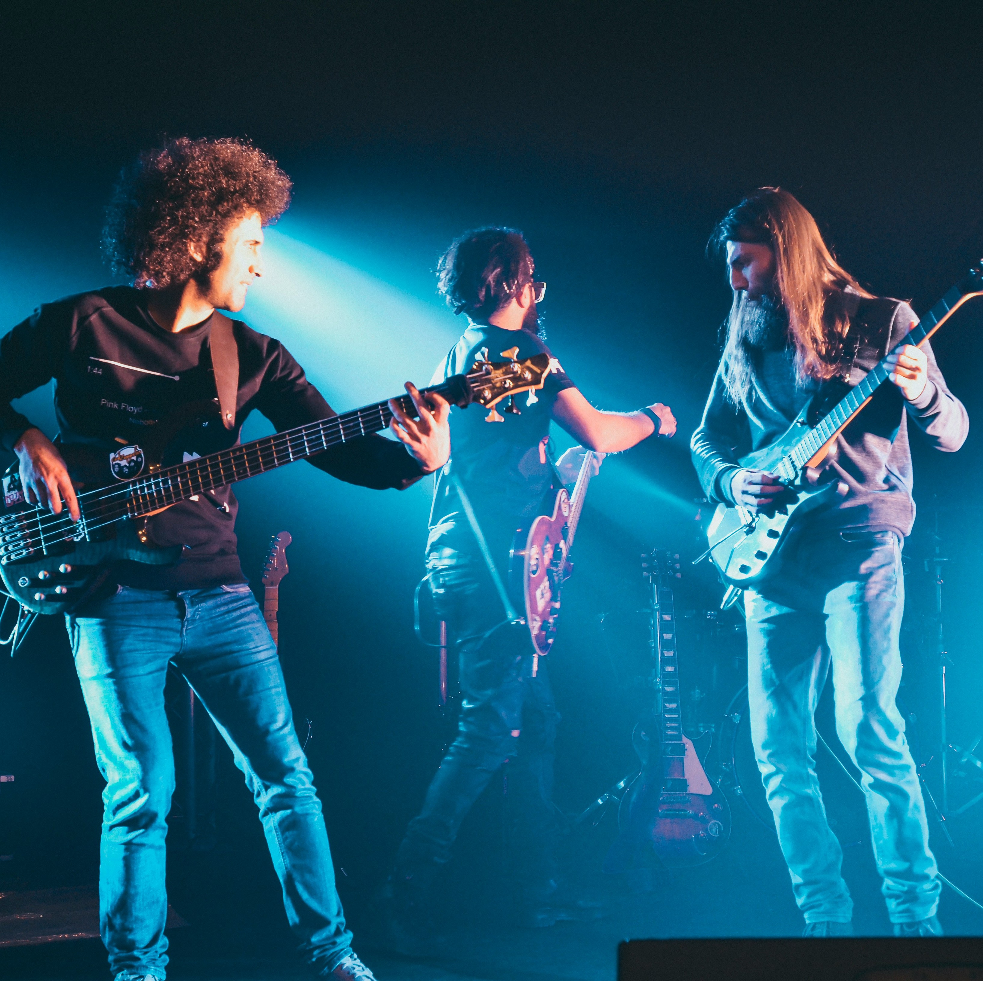 Three guitarists playing on stage under light blue lights