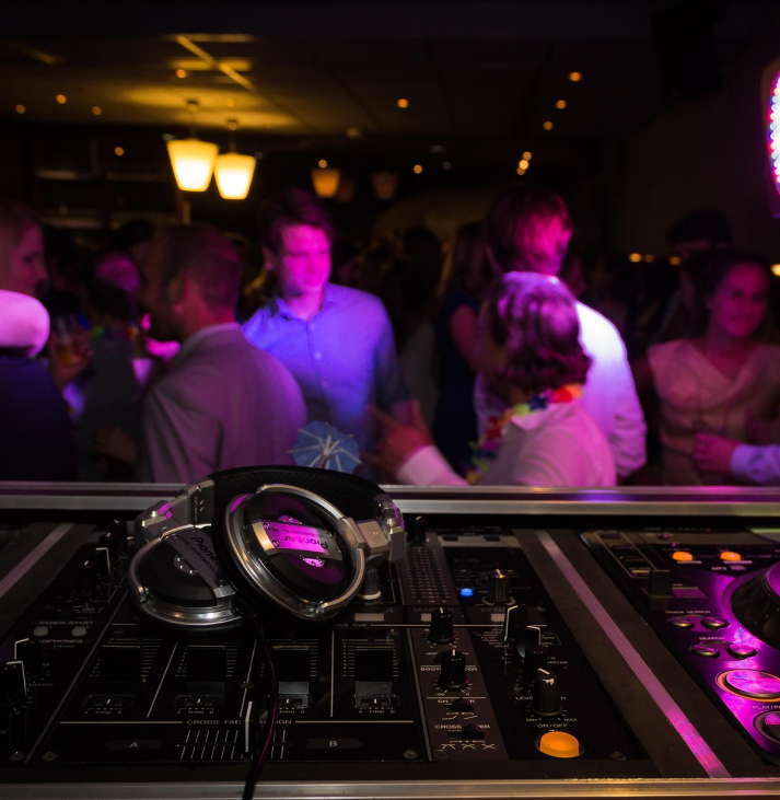 A pair of headphones resting on a dj deck in front of a crowd of people on a dancefloor