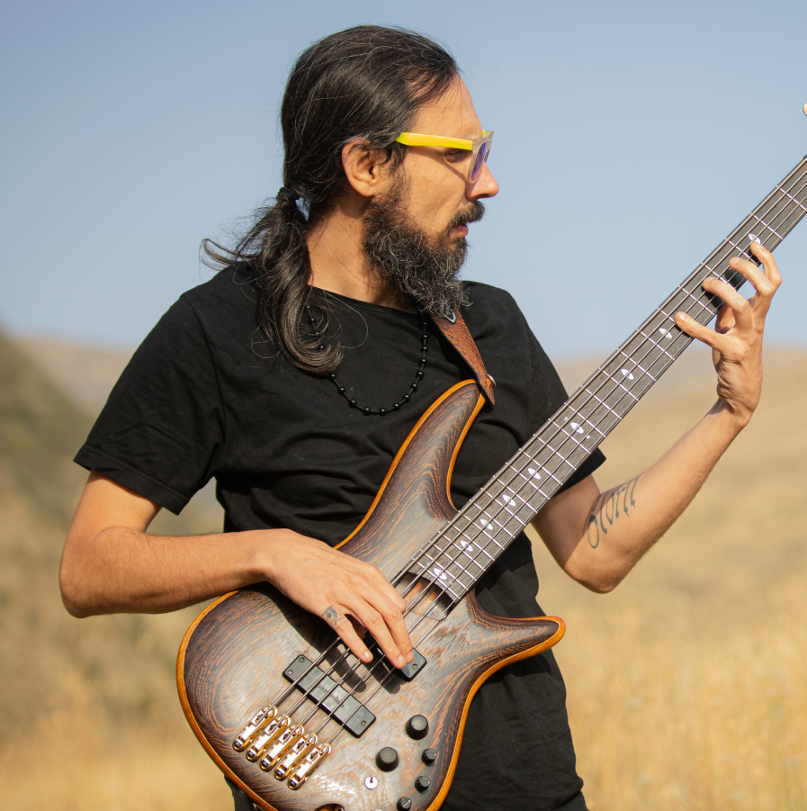 A dark haried man with a ponytail and sunglasses playing an electric guitar
