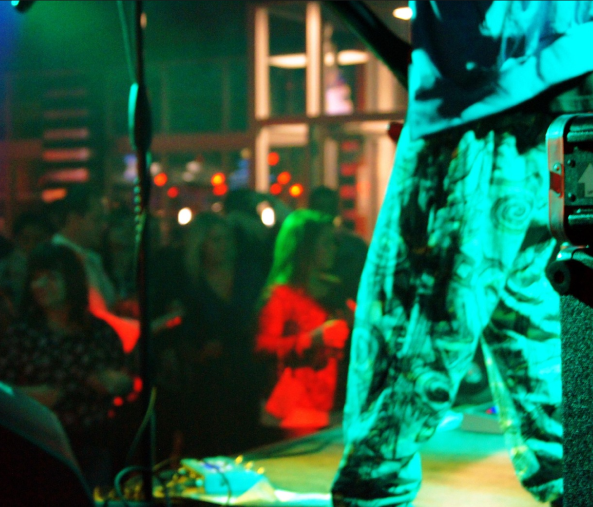 The base of a mic and someones legs standing on a stage under a green light