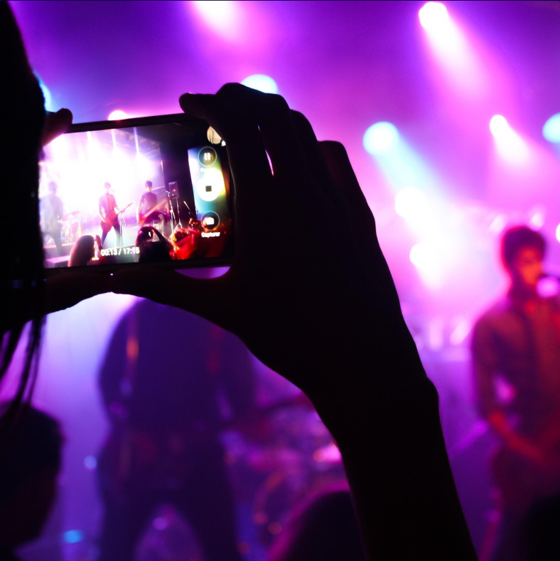 Hands taking a photo on a smartphone of a band standing on a stage